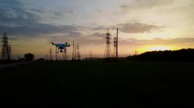 Drone güç hatları üzerinden günbatımında uçar.