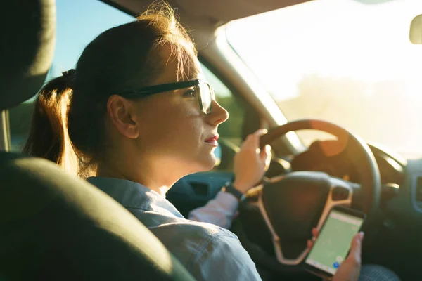 Donna felice utilizza un navigatore in uno smartphone durante la guida di una macchina — Foto Stock