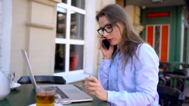 Güzel genç kadın çalışma ve bir kafe açık havada bir akıllı telefon konuşma