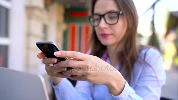 Mooie jonge vrouw met behulp van smartphone in een café in de buitenlucht — Stockvideo