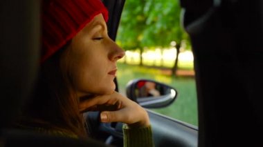 Arabanın yolcu koltuğunda oturan ve güneşli günde pencereden dışarı bakarak mutlu genç kadın