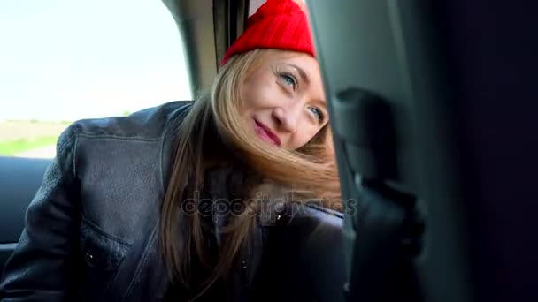 Arabanın yolcu koltuğunda oturan ve güneşli günde pencereden dışarı bakarak mutlu genç kadın — Stok video