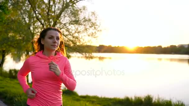 Woman runs through the park on the lake shore at sunset, slow motion — Stock Video