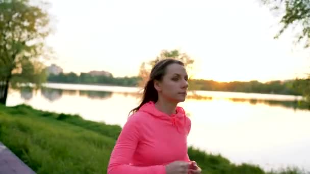 Женщина бежит через парк на берегу озера на закате — стоковое видео