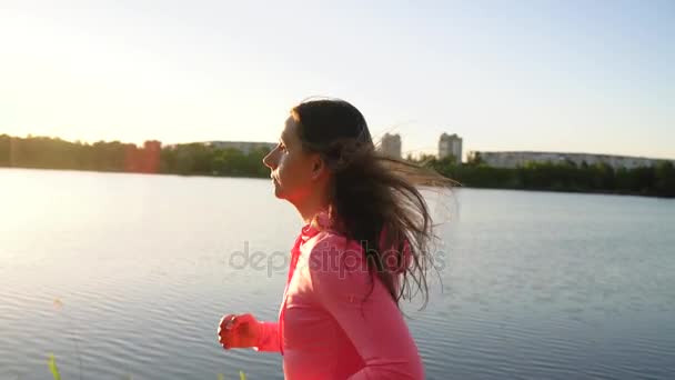 Жінка проходить через парк на березі озера на заході сонця, повільний рух — стокове відео