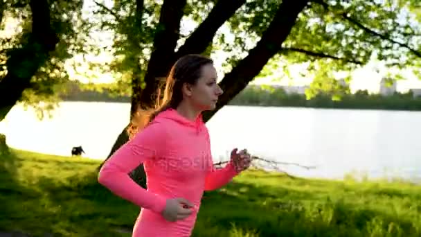 La mujer corre por el parque en la orilla del lago al atardecer, en cámara lenta — Vídeo de stock