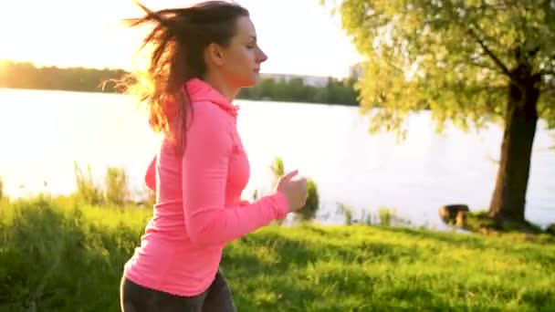 Donna corre attraverso il parco sulla riva del lago al tramonto, al rallentatore — Video Stock