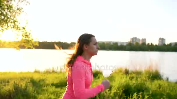 Frau läuft bei Sonnenuntergang durch den Park am Seeufer — Stockvideo