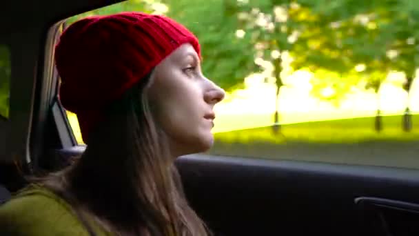 Wanita muda yang bahagia duduk di kursi penumpang mobil dan melihat keluar jendela pada hari yang cerah — Stok Video