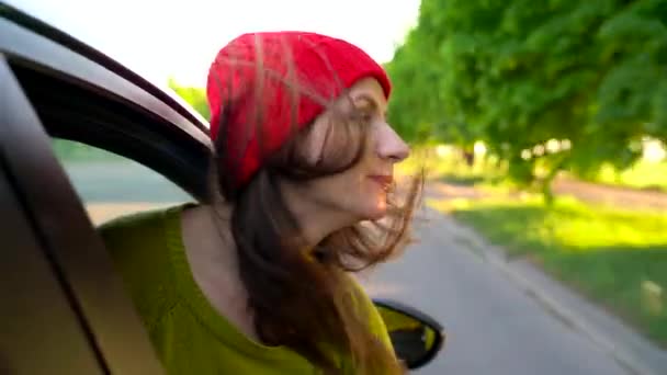 Felice giovane donna seduta sul sedile del passeggero dell'auto e guardando fuori dalla finestra nella giornata di sole — Video Stock