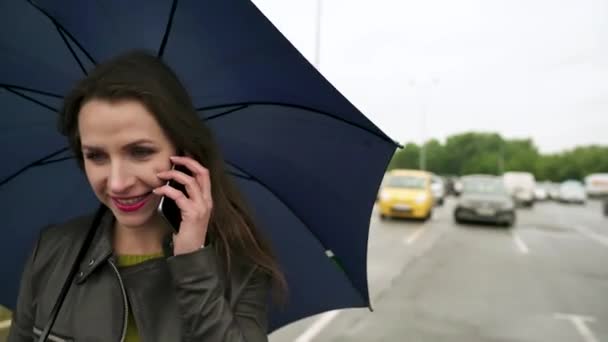 Белая девушка разговаривает по смартфону под зонтиком — стоковое видео
