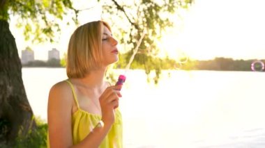 Genç, güzel sarışın dışarıda sabun köpüğü üflüyor.