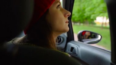 Arabanın yolcu koltuğunda oturan ve güneşli günde pencereden dışarı bakarak mutlu genç kadın