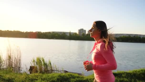 Woman runs through the park on the lake shore at sunset, slow motion — Stock Video