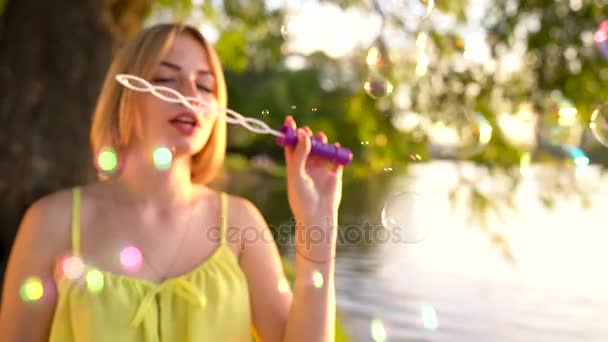 Young beautiful blonde blowing soap bubbles outdoors - slow motion — Stock Video