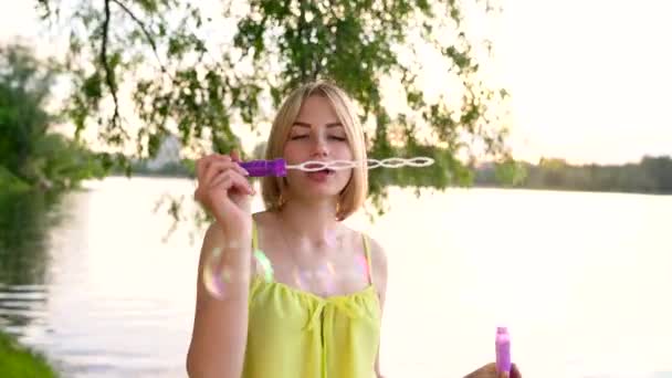 Young beautiful blonde blowing soap bubbles outdoors — Stock Video