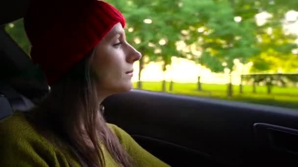 Arabanın yolcu koltuğunda oturan ve güneşli günde pencereden dışarı bakarak mutlu genç kadın — Stok video