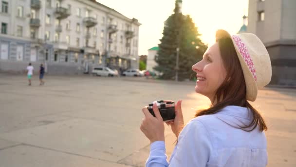 Chica está caminando por la ciudad y tomando fotos de las vistas en una cámara de cine — Vídeos de Stock