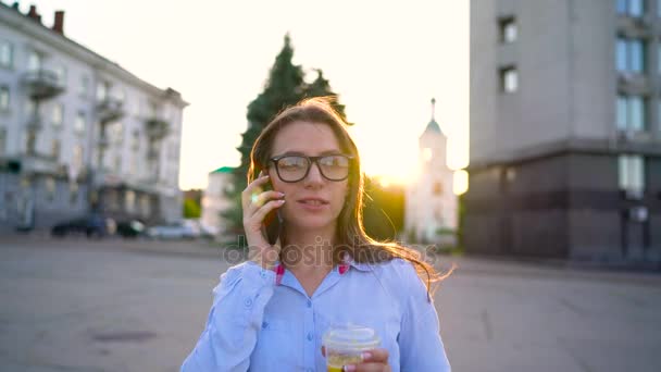 Mujer hablando en smartphone y bebiendo jugo caminando por la calle — Vídeo de stock