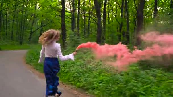 Mujer con ropa hermosa corre por el bosque agitando humo de color, cámara lenta — Vídeo de stock