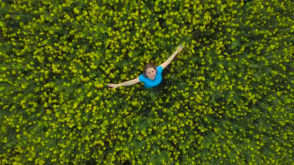 Young woman with arms outstretched in a yellow canola field — Stock Video