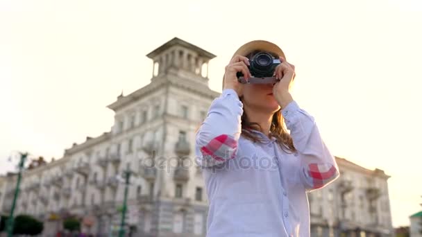 Chica está caminando por la ciudad y tomando fotos de las vistas en una cámara de cine — Vídeos de Stock