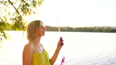 Genç, güzel sarışın dışarıda sabun köpüğü üflüyor.