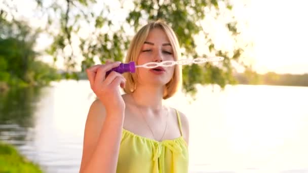 Jovem loira bonita soprando bolhas de sabão ao ar livre - câmera lenta — Vídeo de Stock