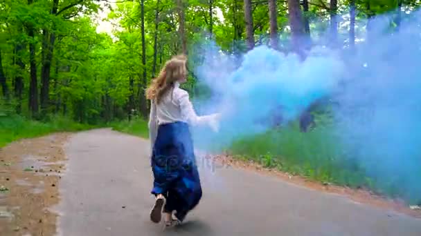 Mujer con ropa hermosa corre por el bosque agitando humo de color — Vídeos de Stock