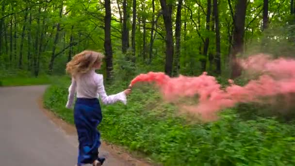 Mujer con ropa hermosa corre por el bosque agitando humo de color, cámara lenta — Vídeo de stock