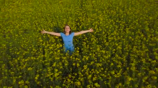 Jeune femme avec les bras tendus dans un champ de canola jaune — Video