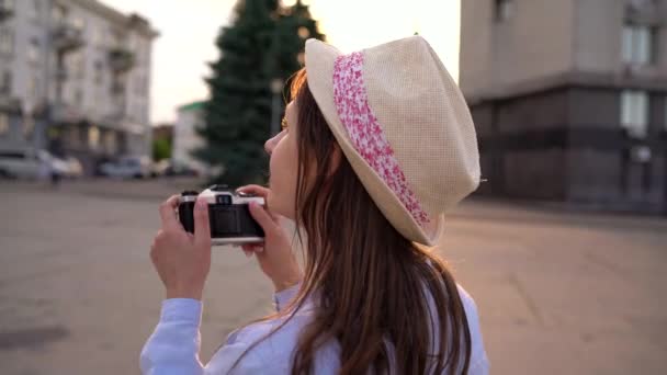 Chica está caminando por la ciudad y tomando fotos de las vistas en una cámara de cine — Vídeos de Stock