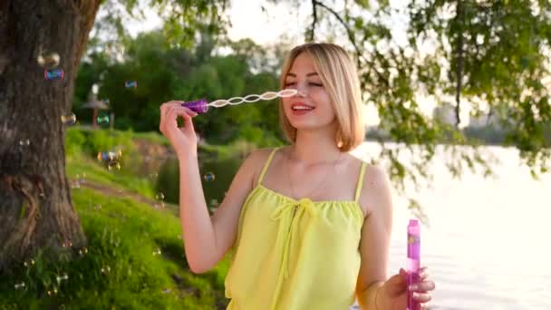 Joven hermosa rubia soplando burbujas de jabón al aire libre — Vídeo de stock