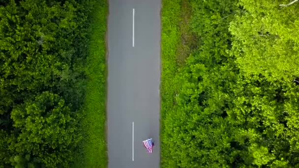 挥舞着美国国旗的少女少妇是滑旱冰的农村的道路上。从山顶 — 图库视频影像