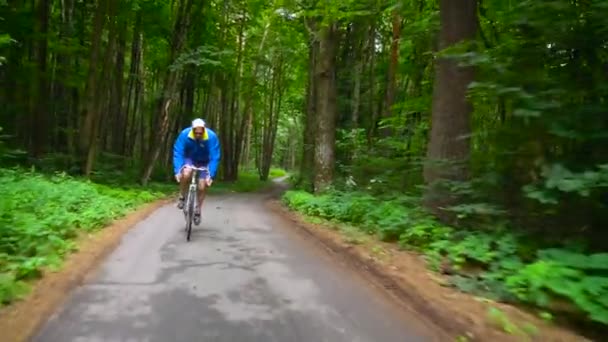 Homem de meia-idade está montando uma bicicleta de estrada ao longo de uma estrada da floresta, câmera lenta — Vídeo de Stock