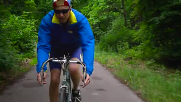 Hombre de mediana edad está montando una bicicleta de carretera a lo largo de un camino forestal — Vídeos de Stock