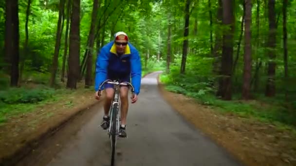 Homem de meia-idade está andando de bicicleta ao longo de uma estrada florestal — Vídeo de Stock