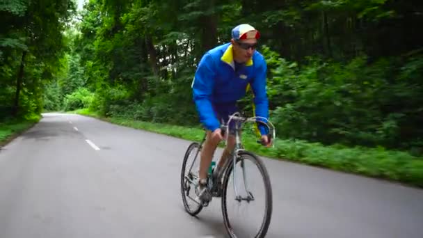 Man van middelbare leeftijd is een racefiets langs een bos weg rijden — Stockvideo