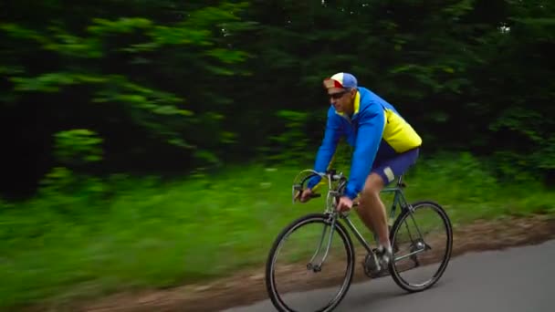 Homem de meia-idade está montando uma bicicleta de estrada ao longo de uma estrada da floresta, câmera lenta — Vídeo de Stock