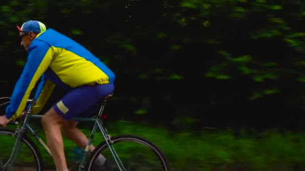 Homem de meia-idade está andando de bicicleta ao longo de uma estrada florestal — Vídeo de Stock