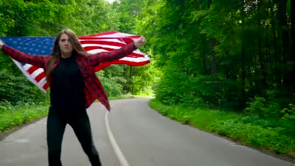 Young teenage woman waving a US flag is roller skating through woods. Slow motion — Stock Video