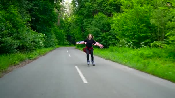 Wanita muda melambaikan bendera AS adalah roller skating melalui hutan. Gerakan lambat — Stok Video