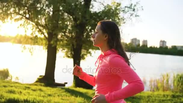 Donna corre attraverso il parco sulla riva del lago al tramonto, al rallentatore — Video Stock