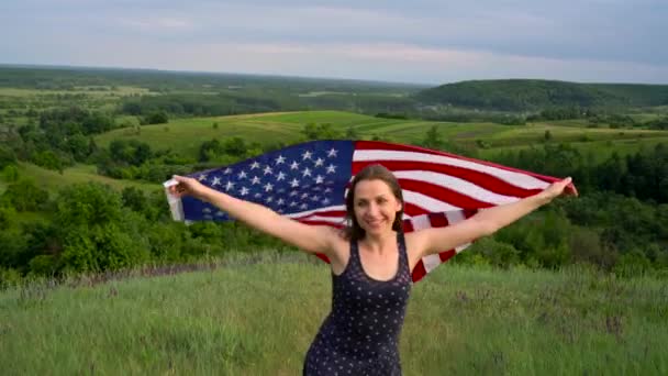 Une femme agitant un drapeau américain se tient au sommet d'une colline - le concept du Jour de l'indépendance États-Unis — Video