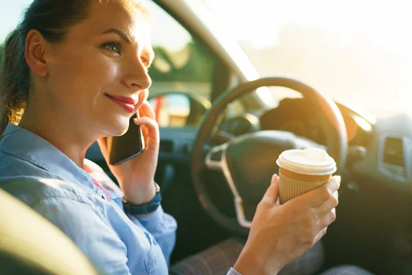 Mujer joven hablando en un teléfono inteligente y beber café mientras dr — Foto de Stock