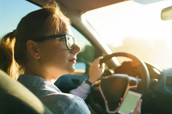 Mujer feliz utiliza un navegador en un teléfono inteligente mientras conduce un coche — Foto de Stock