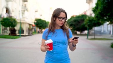 Kadın smartphone ve içme kahve sokakta yürürken kullanır. Ağır çekim