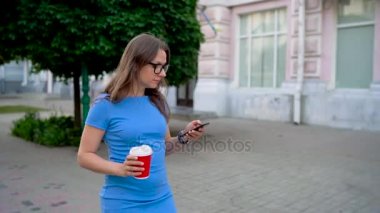 Kadın smartphone ve içme kahve sokakta yürürken kullanır