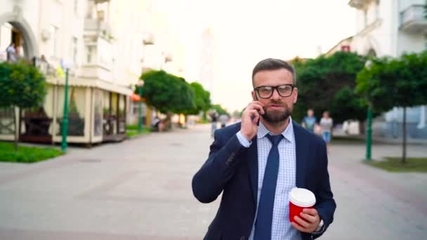 Ο άνθρωπος μιλά στο smartphone και πίνοντας καφέ το περπάτημα κάτω από την οδό — Αρχείο Βίντεο