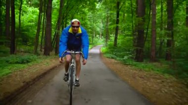 Orta yaşlı adam ağır çekim bir orman yolu boyunca bir yol bisikleti biniyor